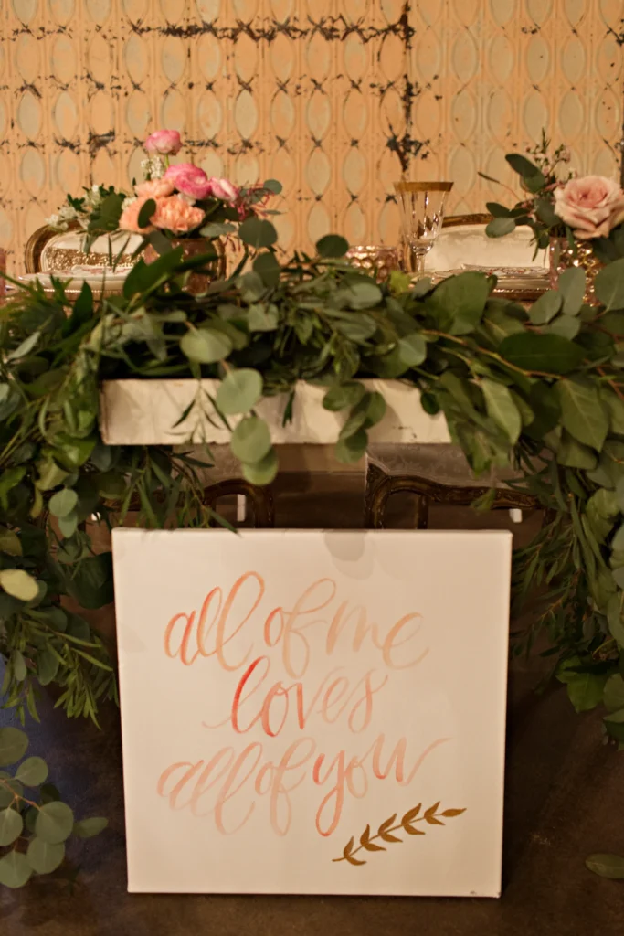 Sweetheart table with gold-rimmed glassware, pink florals, and eucalyptus garland